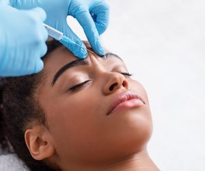 Plastic surgery_ Young african woman receiving botox injection in interbrow zone at beauty